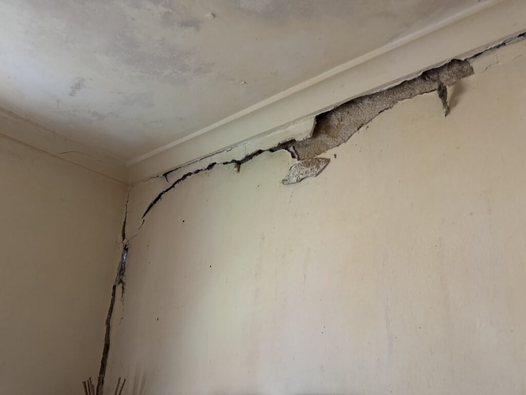 wall displaying a crack and a ceiling hole, highlighting possible structural engineering problems.