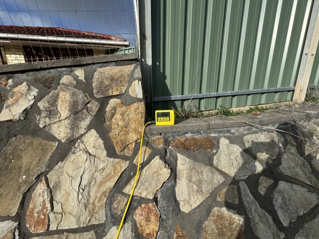 A yellow electric meter mounted on a stone retaining wall.